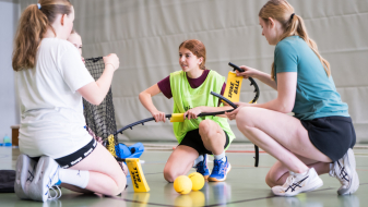Junge Frauen in einer Halle in einem Kreis, sie bauen einen Spikeball zusammen