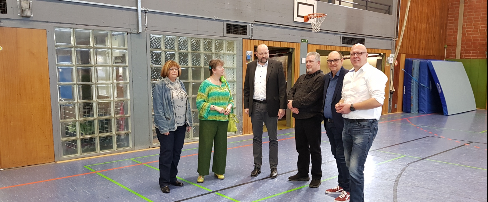 Staatssekretärin steht mit Mitgliedern des Handballvereins in einer Sporthalle.