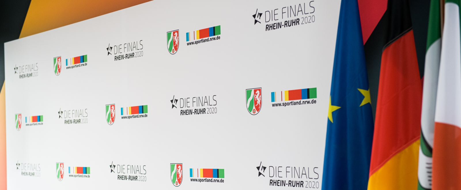 Weiße Plakatwand mit vielen NRW-Wappen, Sportland.NRW-Logos und Finals-Logos, rechts sieht man die Flaggen von Europa, Deutschalnd und NRW.