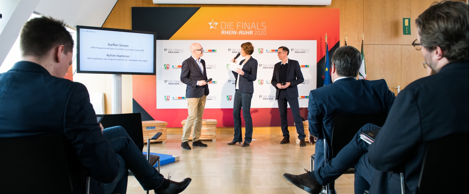 Drei Personen stehen vor einer weißen Plakatwand, links und rechts sieht man einige sitzende Zuschauer, rechts vorne Ministerpräsident Armin Laschet, direkt dahinter der Regierungssprecher Christian Wiermer.