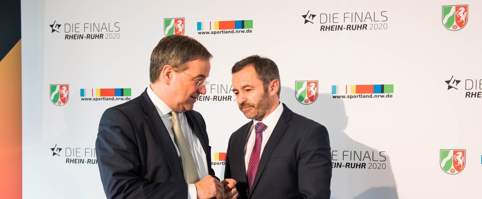 MInisterpräsident Laschet steht mit einem Herrn vor einer weißen Plakatwand.