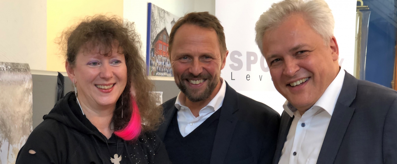 Staatssekretärin Milz steht links neben zwei Herren von der Stadt Leverkusen, gemeinsam halten sie den Zuwendungsbescheid.