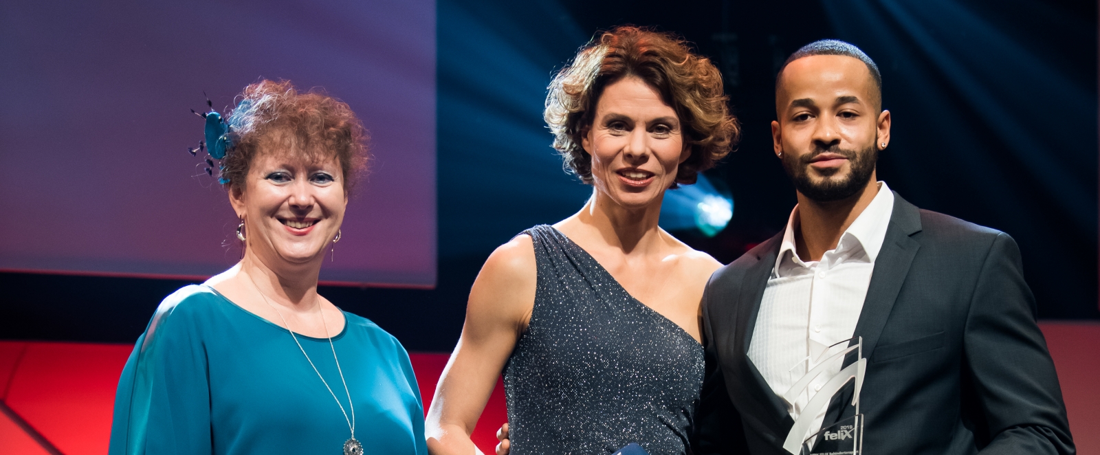 Links steht Staatssekretärin Andrea Milz im dunkelgrünen Kleid, in der Mittte die Moderatorin und rechts von ihr steht Leon Schäfer mit einem Felix-Award in seiner linken Hand.