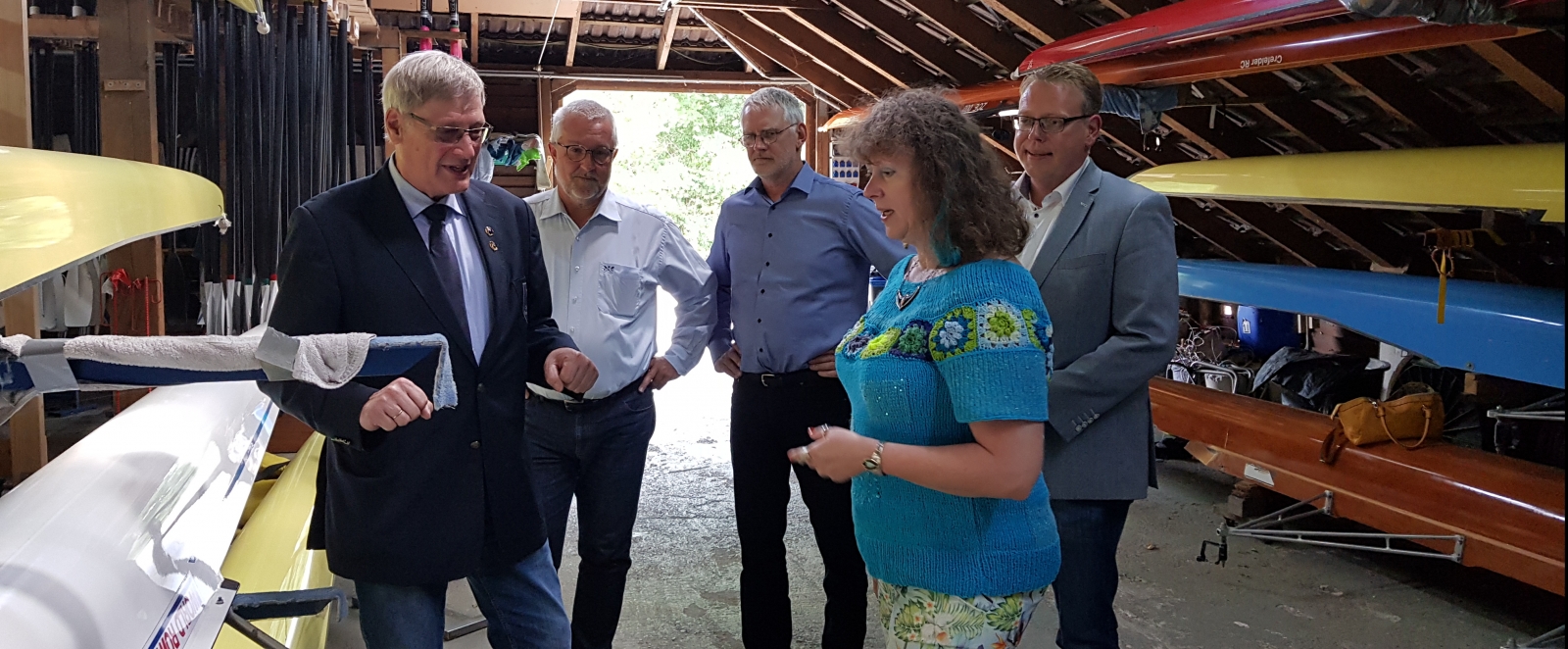 Staatssekretärin Milz mit Vereinsmitgliedern in einem Ruderbootshaus.