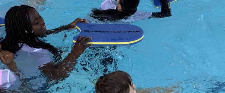Ein Kind im Schwimmbad mit einem Schwimmbrett mit der Aufschrift #SchwimmenLernenNRW