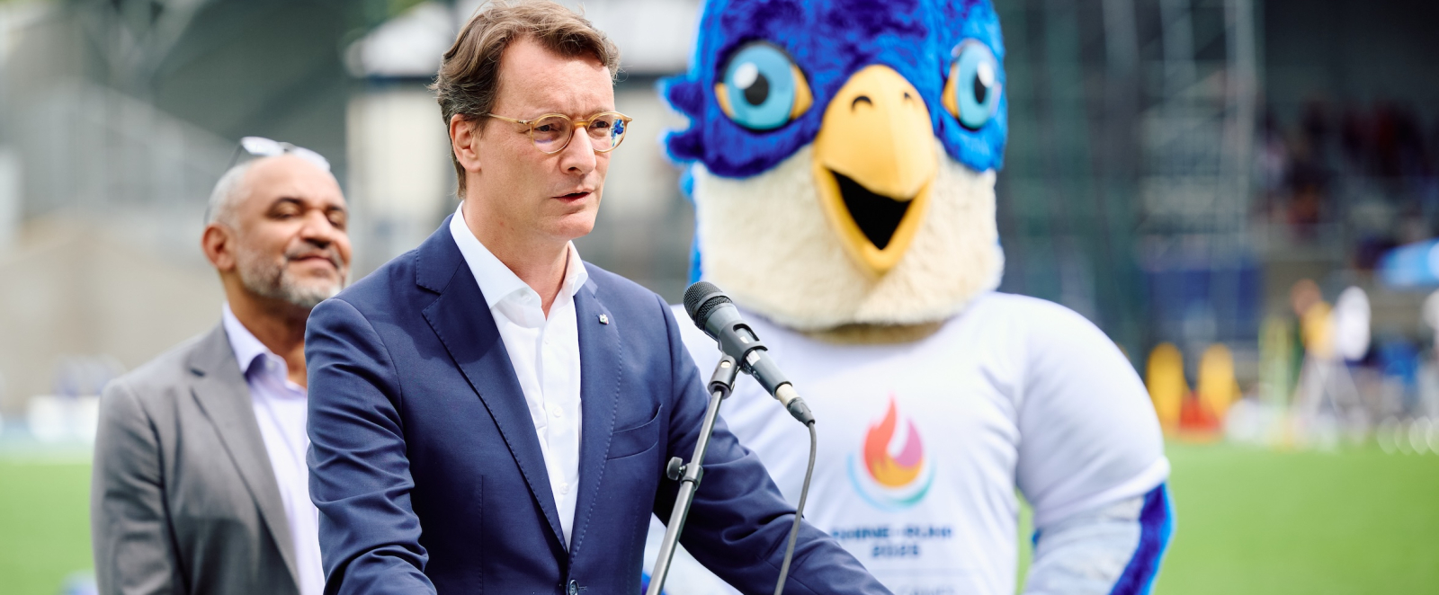 Hendrik Wüst am Mikrofon mit Maskottchen