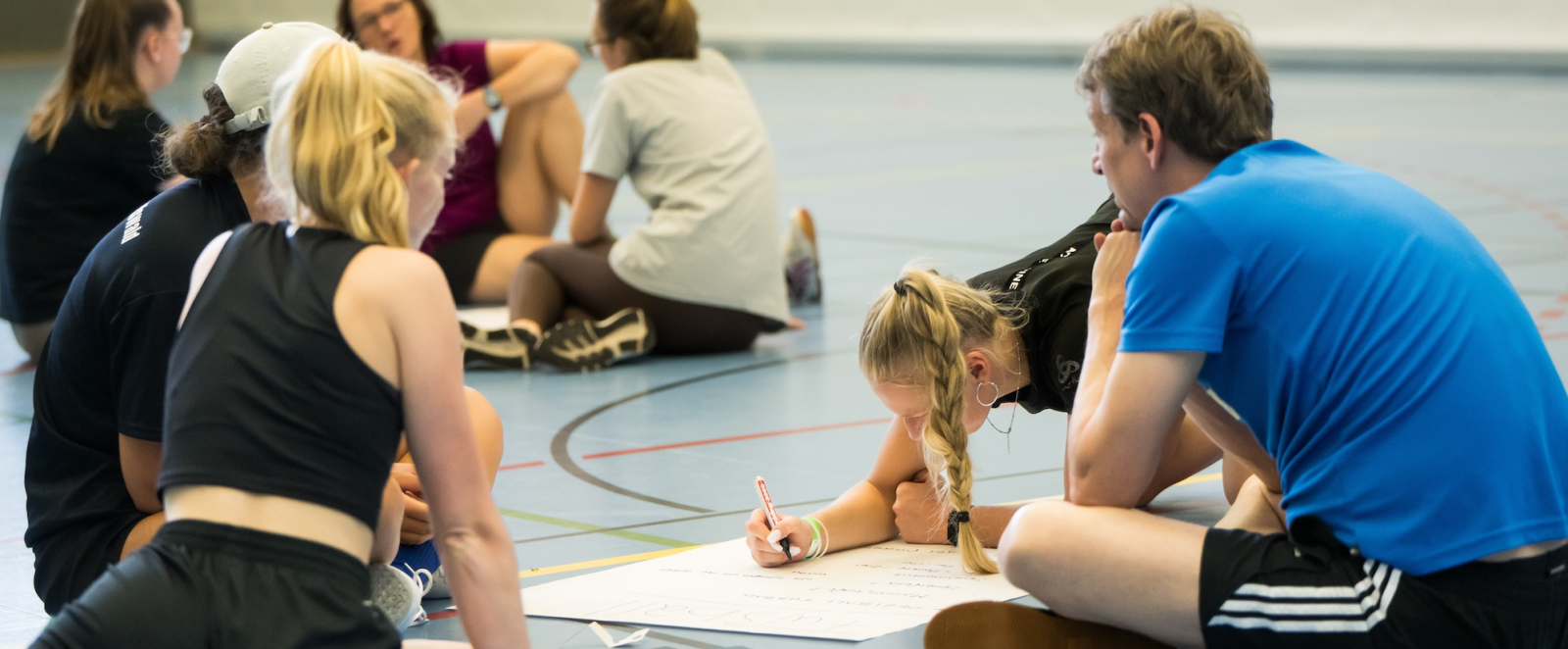 Junge Menschen in einer Sportalle beugen sich über ein Papier