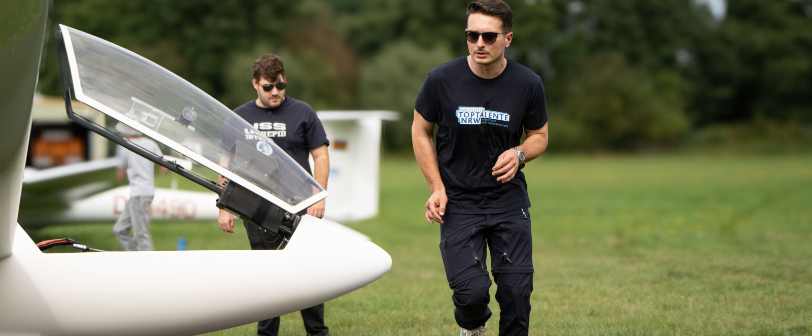 Zwei Personen in schwarzer Kleidung bei einem Segelflugzeug am boden