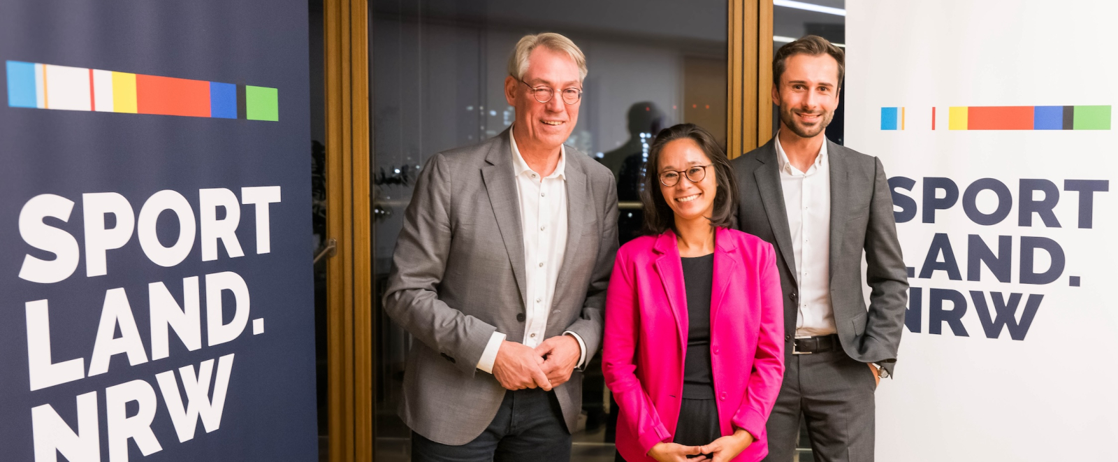 Drei Personen zwischen Sportland.NRW-Bannern