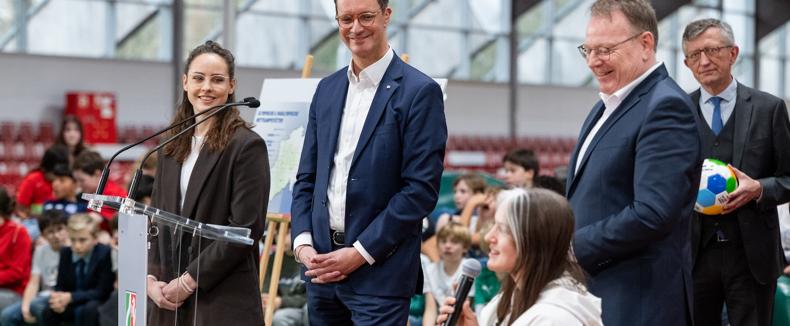Rollstuhlfahrerin mit einem Mikrofon in der Hand neben Hendrik Wüst 