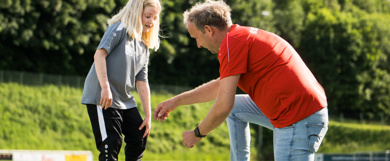 Junger Übungleiter kniet vor einer jungen Sportlerin und erklärt etwas