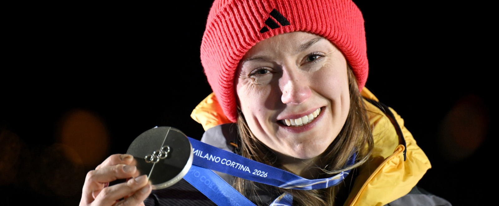 Laura Nolte mit roter Mütze, hält Silbermedaille, vor dunklem Hintergrund