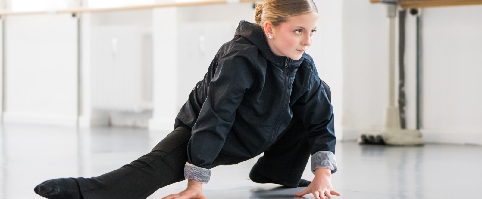 Junge Frau in dunkler Kleidung in Tanzpose mit Händen auf Boden eines Studios
