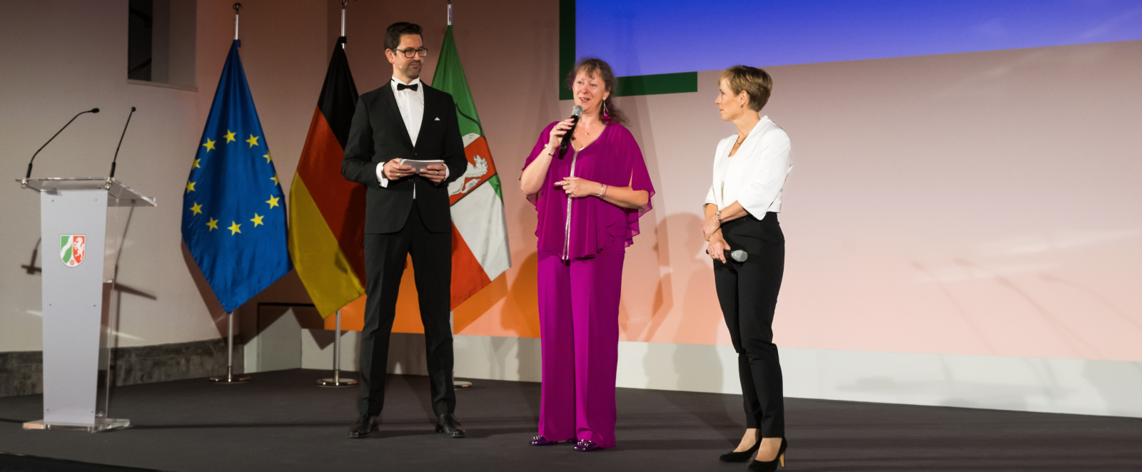 Redner auf einer Bühne mit Andrea Milz in der Mitte und Eva Selic rechts