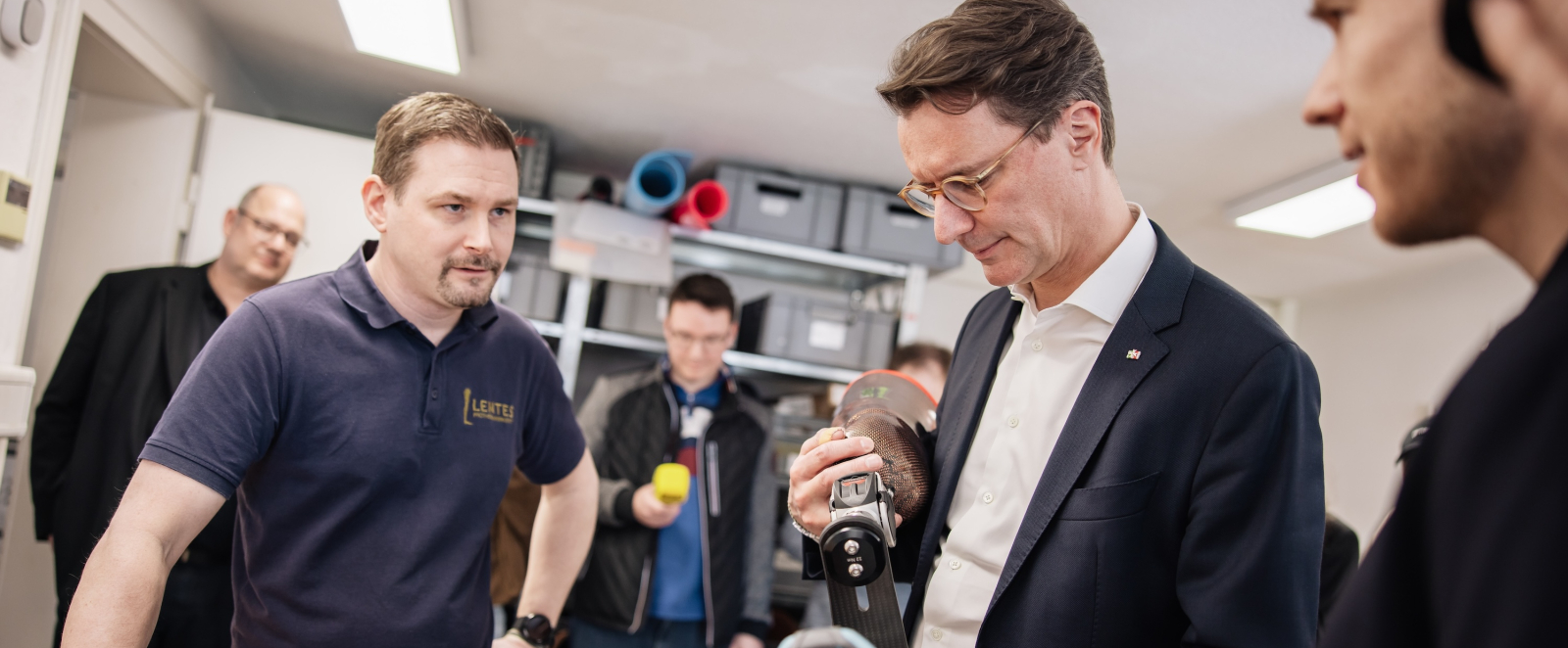 Hendrik Wüst lässt sich eine Prothese in der Werkstatt zeigen, mehrere Personen stehen daneben