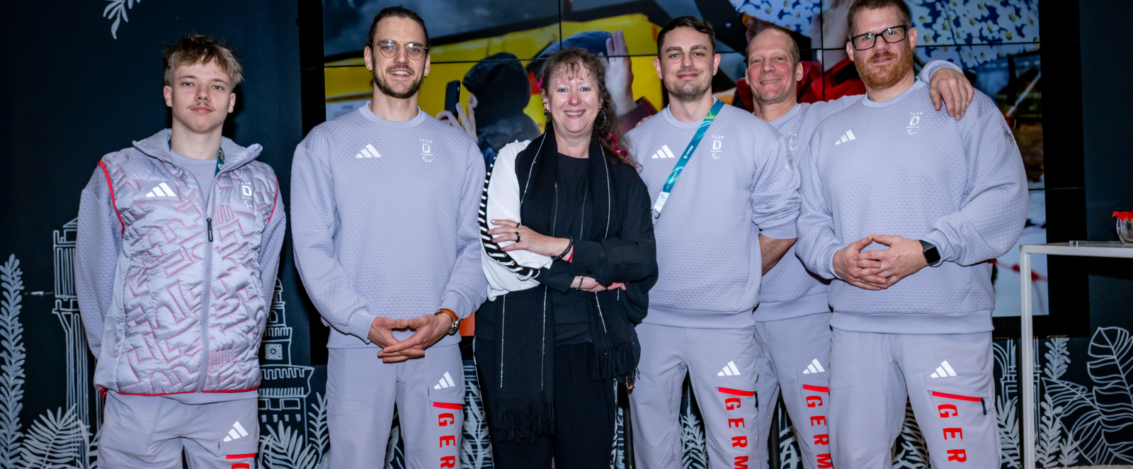 Andrea Milz, umgeben von den NRW-Para Eishockeyspielern bei den Paraylmpics 2026