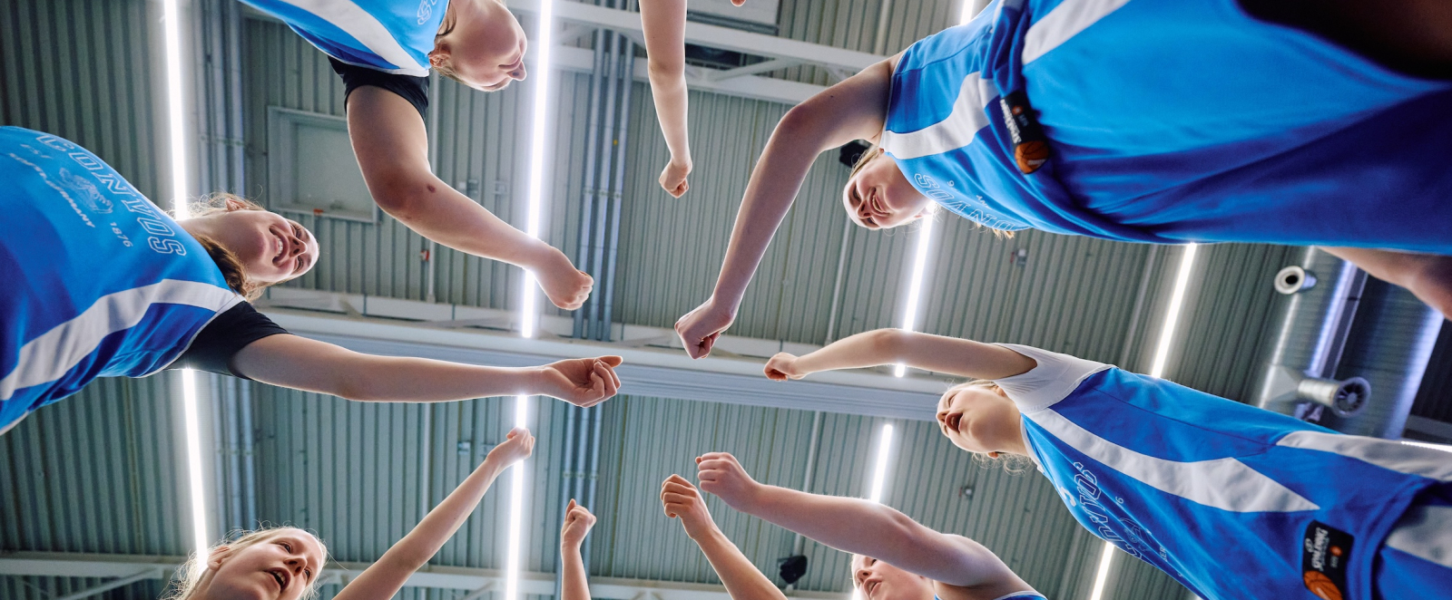 Ein Kreis aus Händen von Jugendlichen in blauen Trikots, von unten aufgenommen