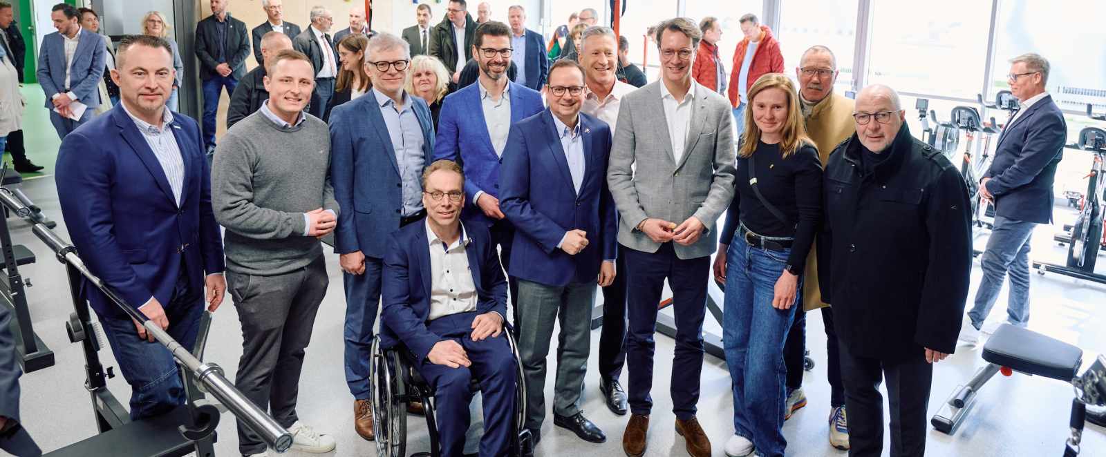 Ministerpräsident Wüst inmitten von Personen, davon eine im Rollstuhl, in einem Raum mit Fenstern im Hintergrund