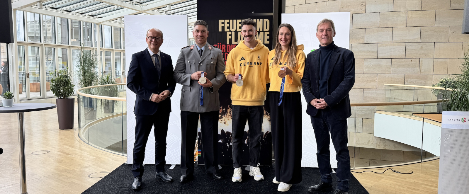 Mehrere Personen auf einem schwarzen Podium bei der Ausstellungseröffnung im Landtag NRW