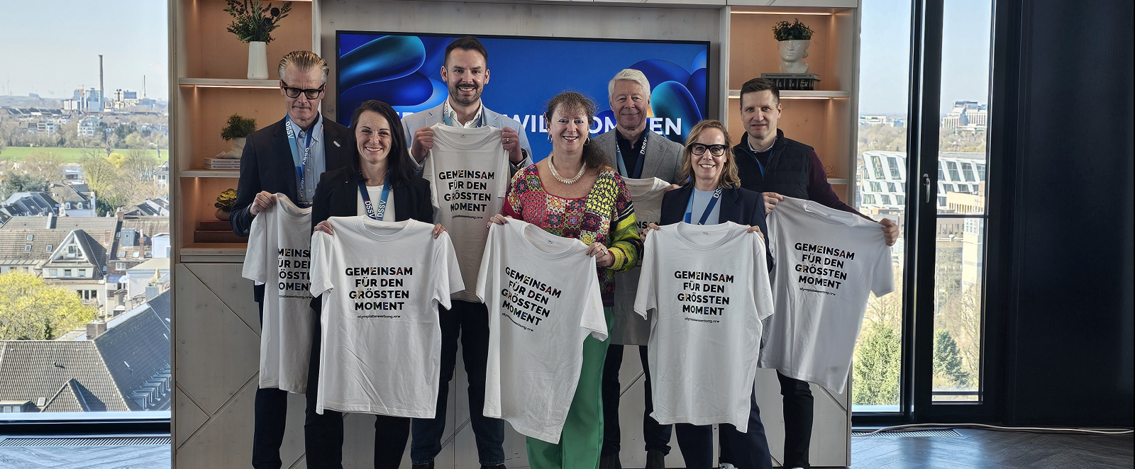 Mehrere Personen halten helle T-Shirts hoch, im Hintergrund Fenster
