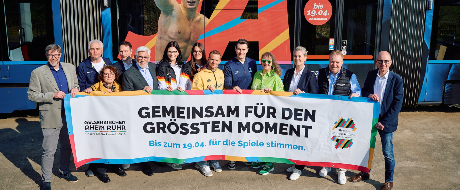 Andrea Milz mit weiteren Personen halten ein Banner der KRR-Bewerbung vor einer speziell beklebten Straßenbahn