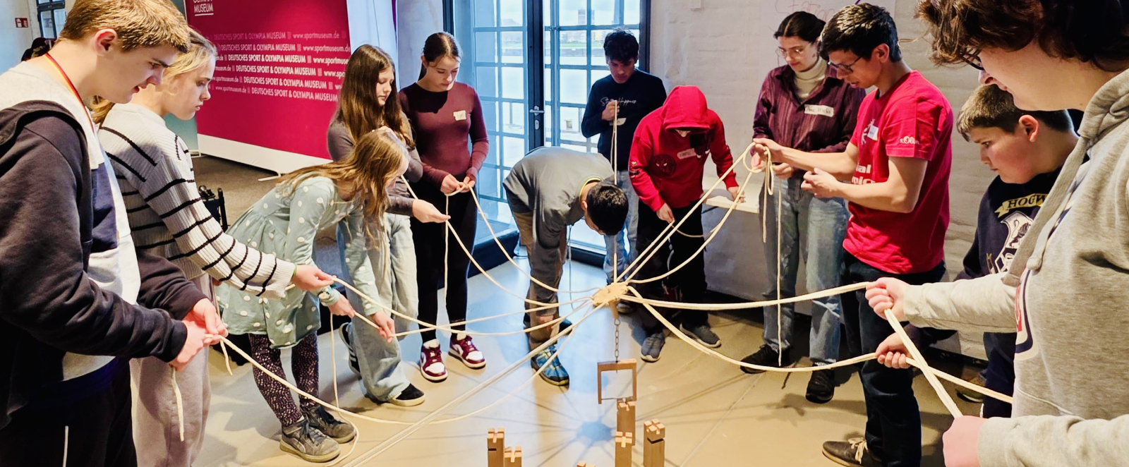 Schüler in einem Innenraum mit hohen Decken, hellem Boden und einem großen Fenster im Hintergrund
