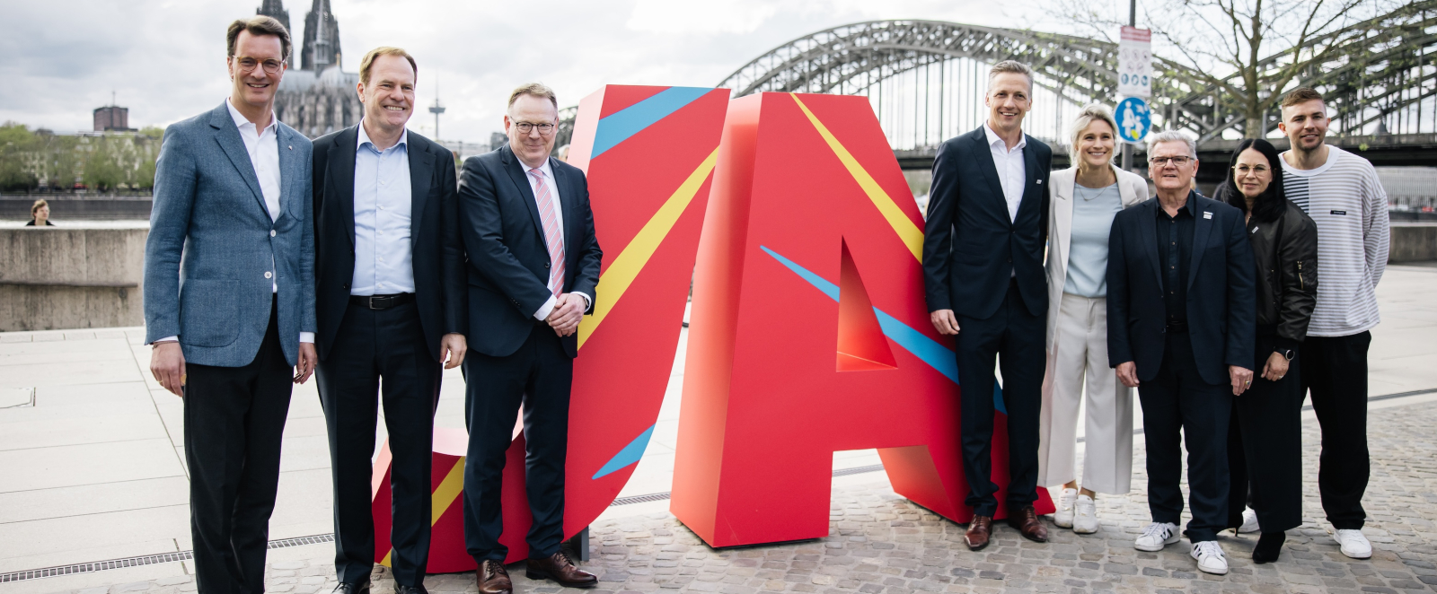 Eine Gruppe von Menschen steht vor großen bunten Buchstaben "JA" im Hintergrund eine Brücke