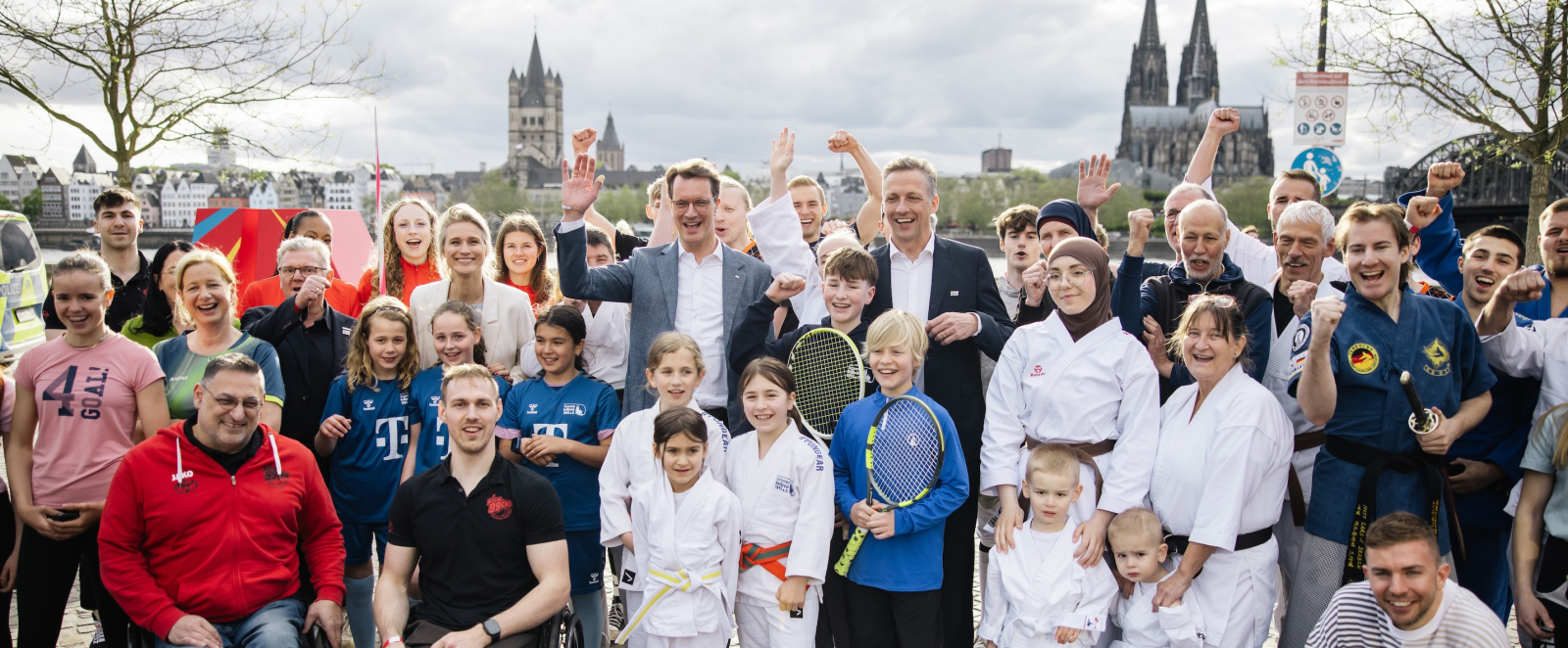 Ministerpräsident Wüst inmitten einer bunten Gruppe von Menschen vor der Skyline von Köln