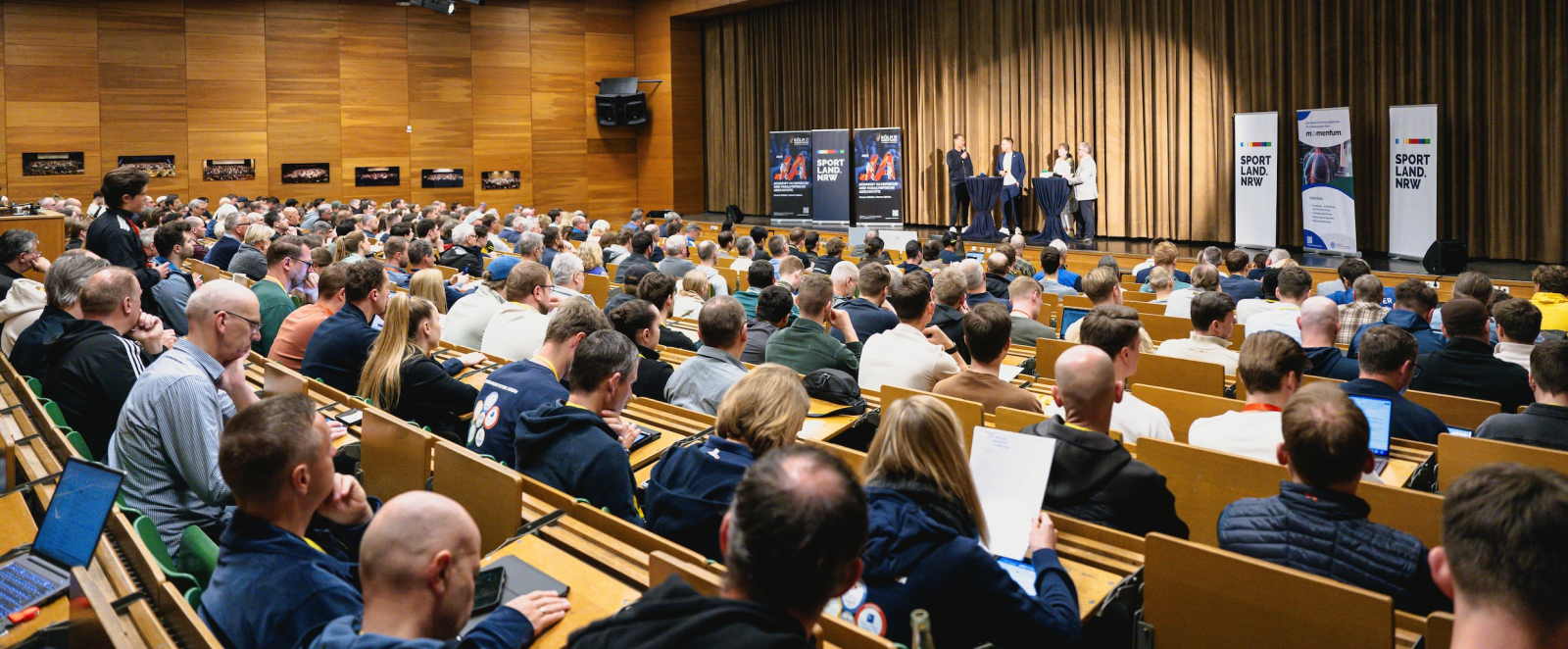 Blick über besetzte Stuhlreihen auf eine Bühne