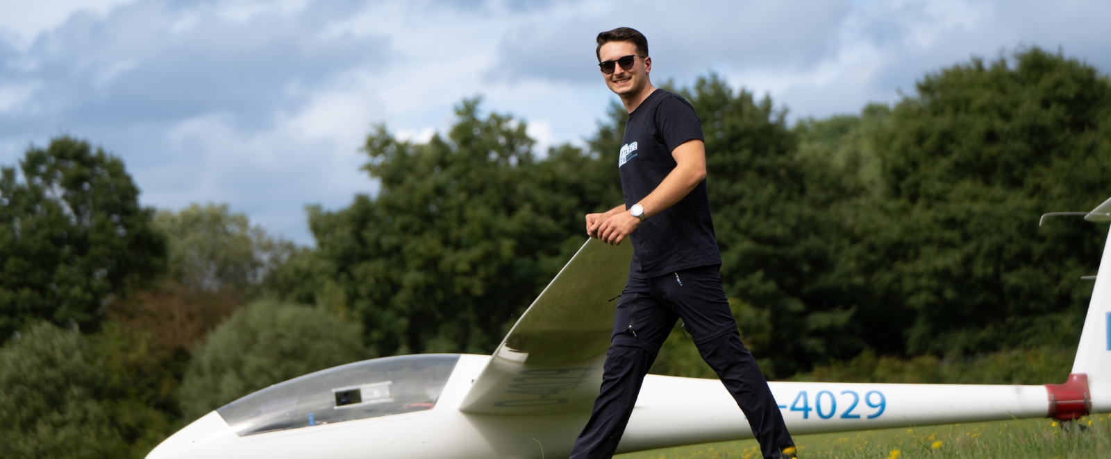 Junger Mann in dunkler Kleidung vor einem am Boden liegenden weißen Segelflugzeug