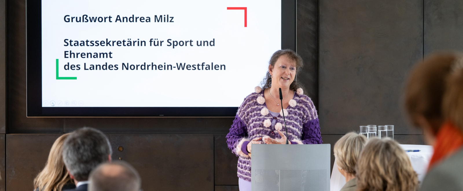 Andrea Milz an einem Pult, hinter ihr steht auf einem Bildschirm "Grußwort Andrea Milz" 