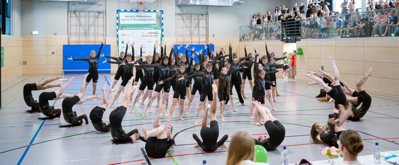 Eine Gruppe Kunstturnerinnen in schwarzen Outfits bei einer Aufführung in einer Sporthalle