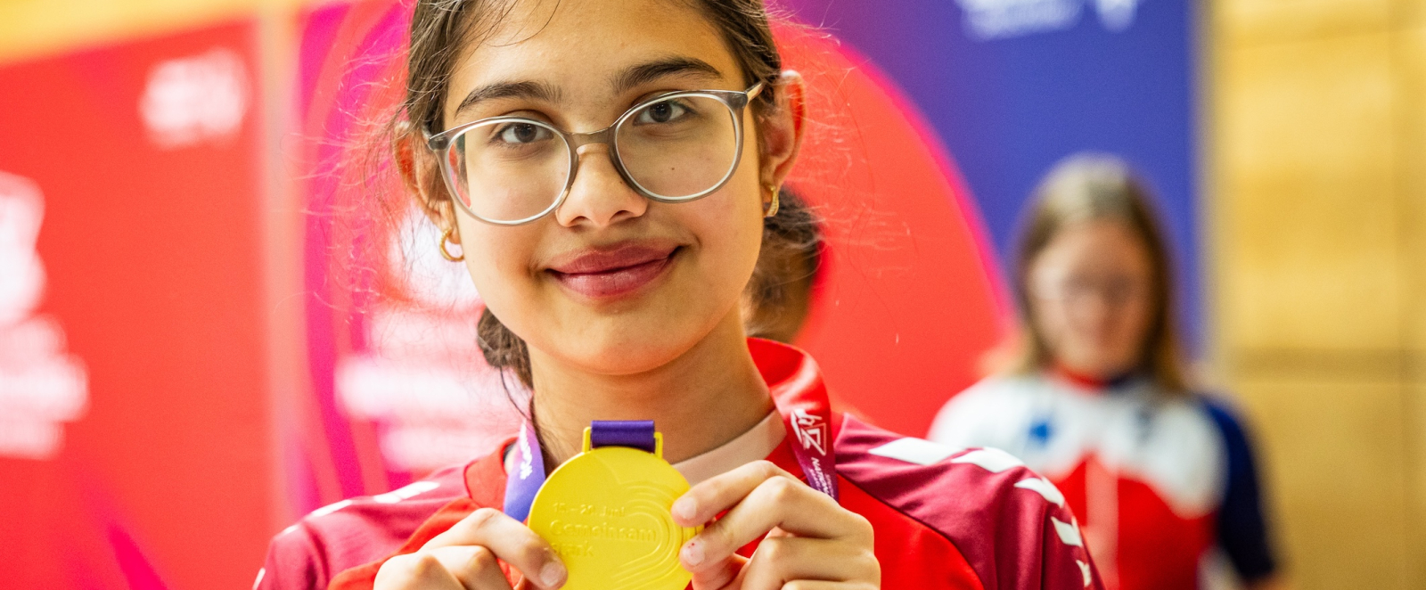 Junge Sportlerin mit Brille zeigt ihre Medaille