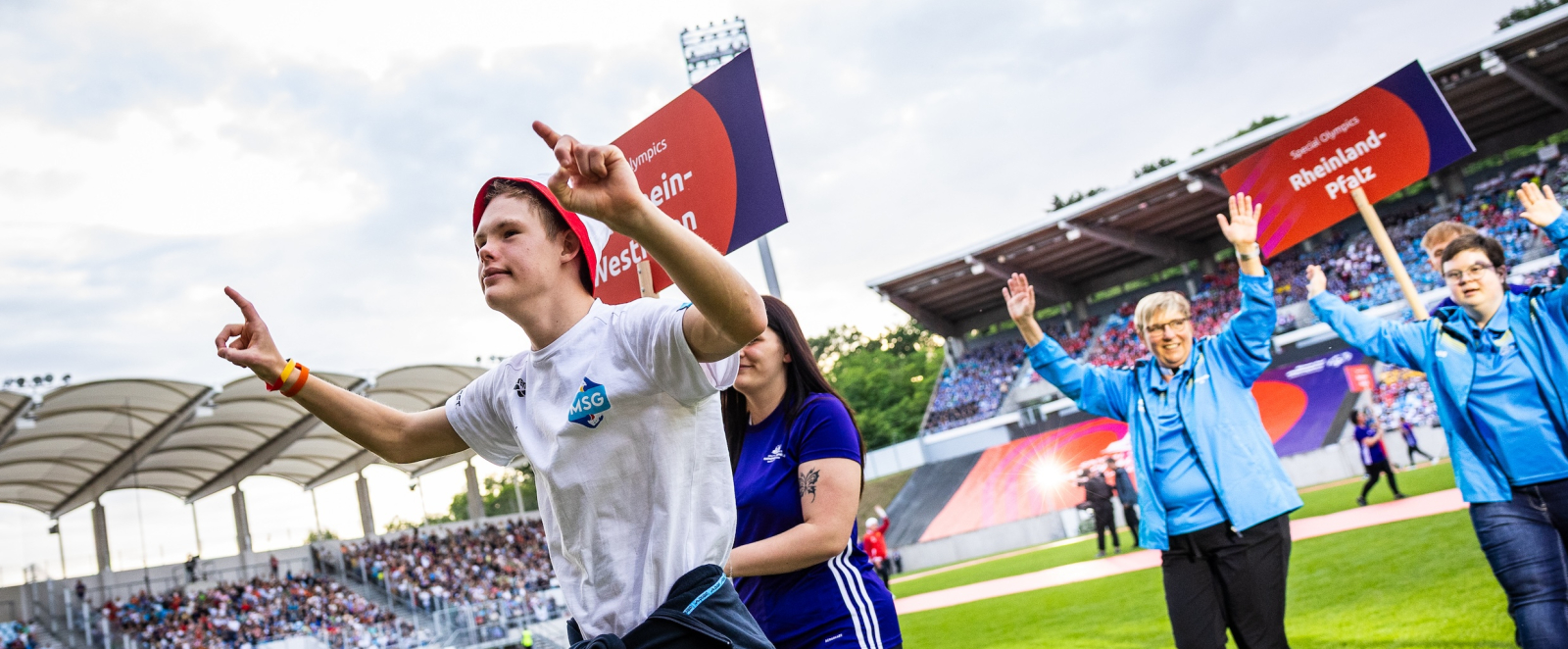 Einlauf von Personen in ein Stadion mit grünem Rasen, eine Person hält das Schild der NRW-Delegation