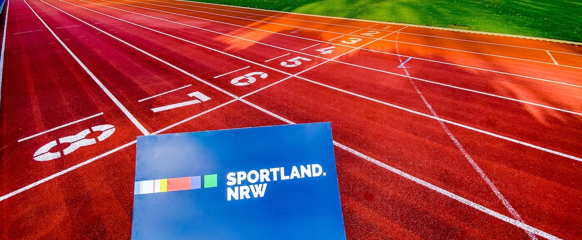 Blaues Schild mit Aufschrift "Sportland.NRW" liegt auf einer roten Tartanbahn