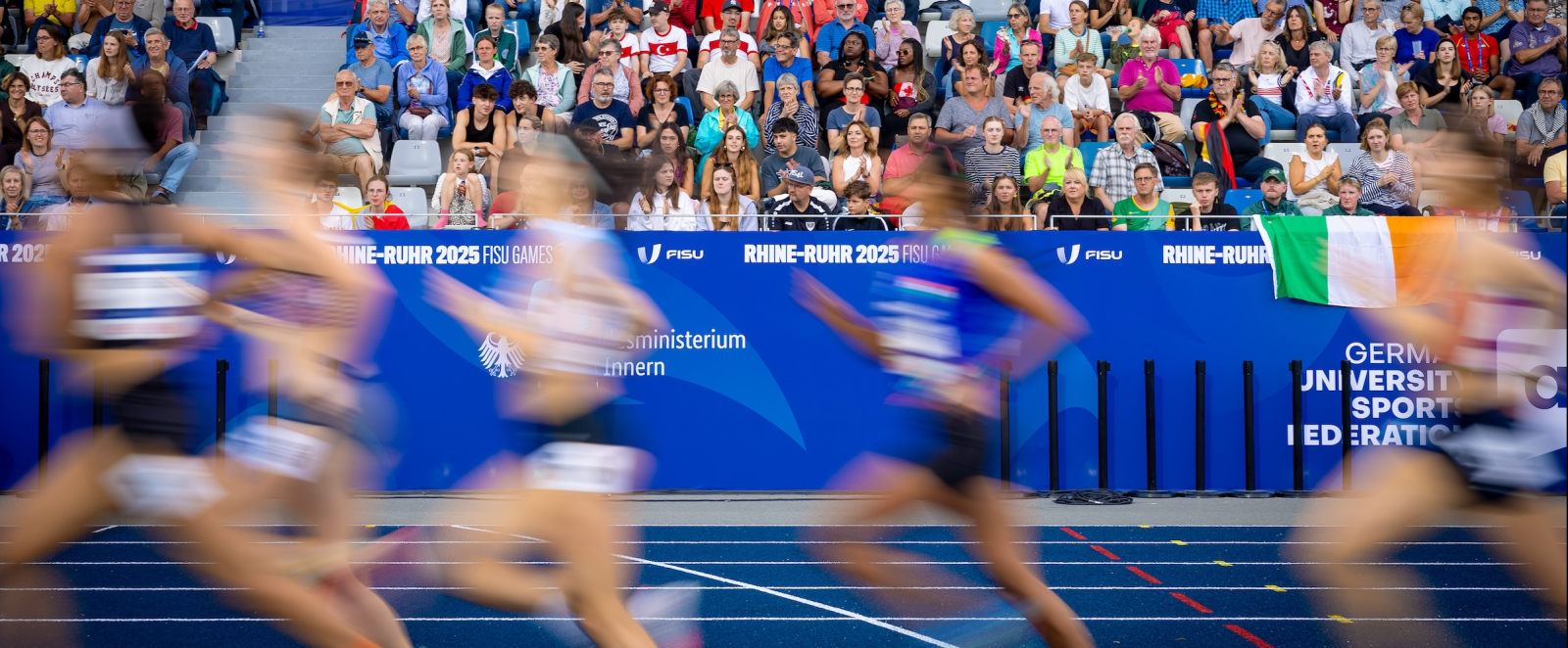 Sportlerinnen in einem Stadion laufen vor voll besetzter Zuschauertribüne