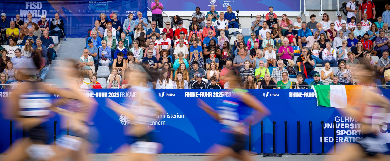 Sportlerinnen in einem Stadion laufen vor voll besetzter Zuschauertribüne