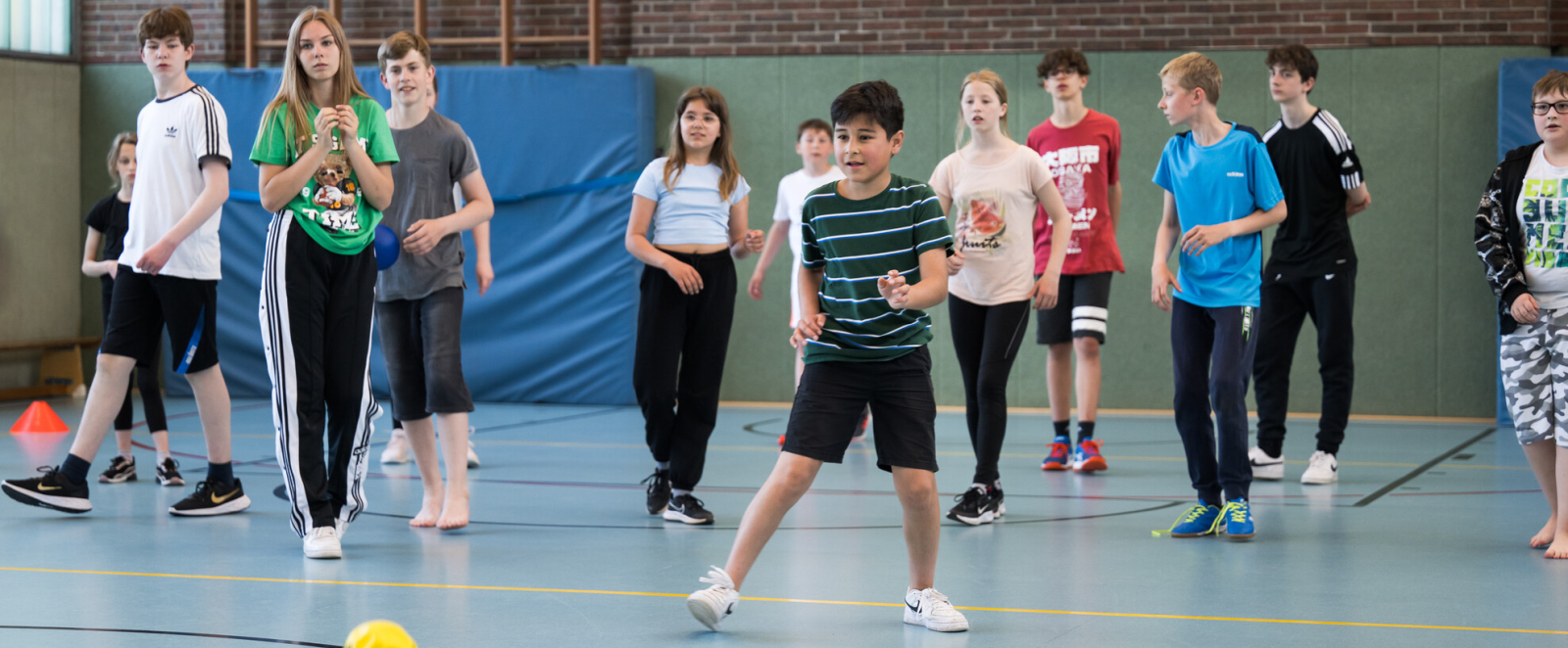 Schulkinder in einer Turhalle, ein gelber Ball im Vordergrund