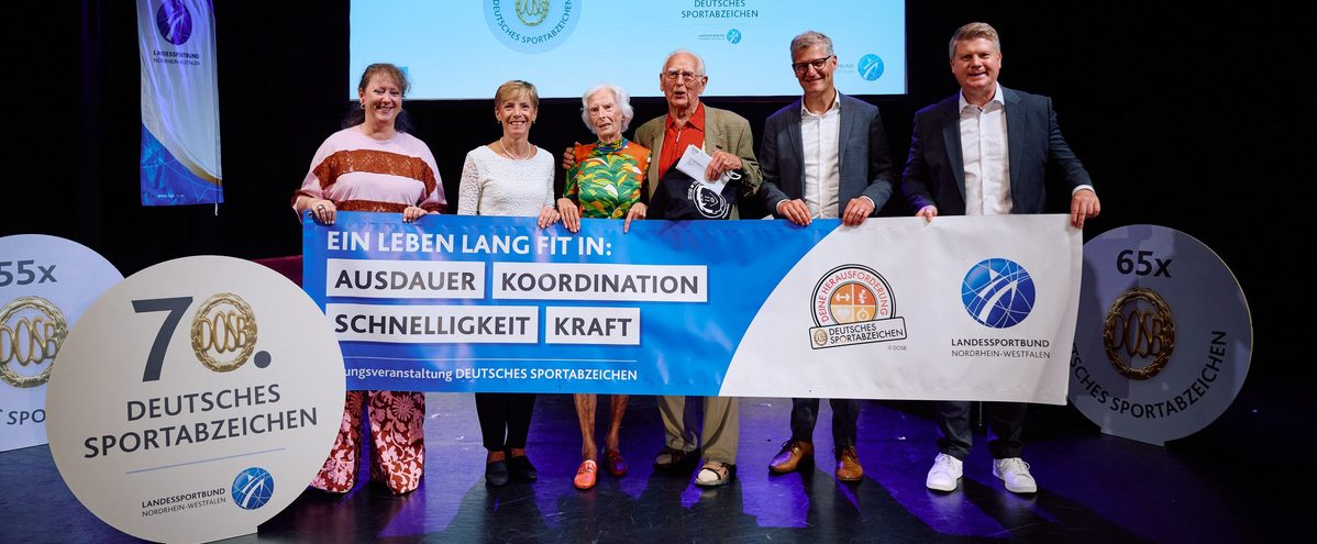 Sechs Personen halten einen Banner auf einer Bühne