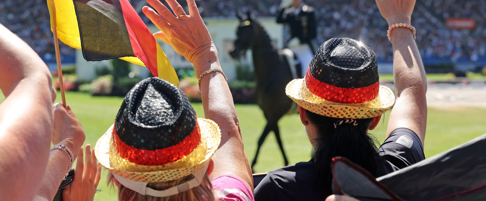 Fans mit Hut in Deutschlandfahnen winken einem Reiter zu