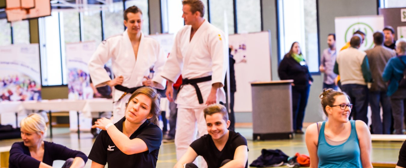 Gruppe junger Frauen und Männer in einer Halle, einige davon in Judo-Dress