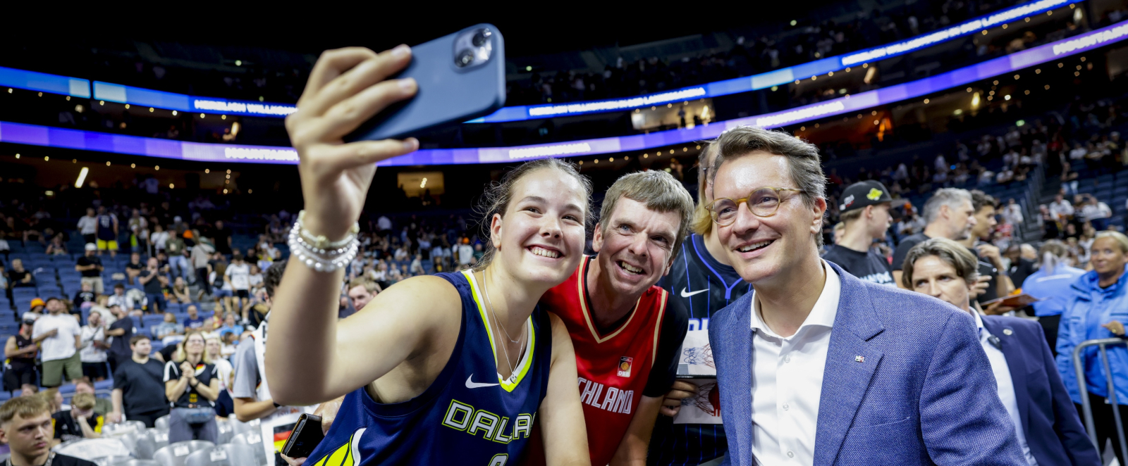 Ministerpräsident in einer vollbesetzten Halle, macht Selfie mit Basketballern