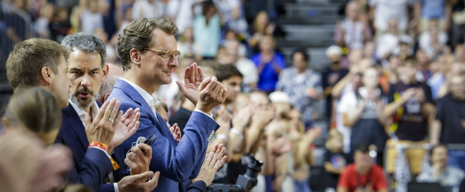 Ministerpräsident Wüst auf voll besetzter Tribüne, er klatscht