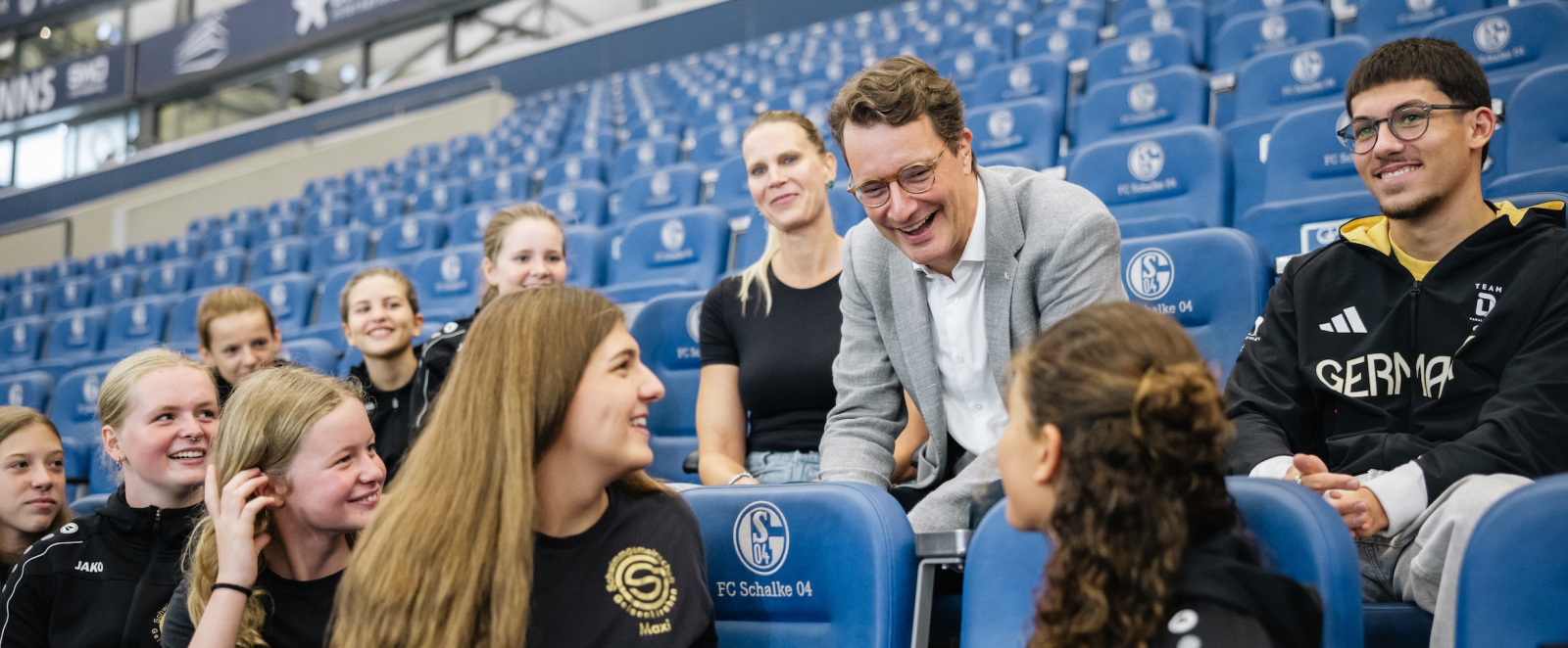 Ministerpräsident Wüst unterhält sich mit weiteren Menschen auf einer Tribüne