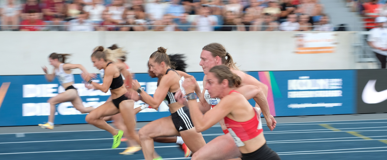 Sportlerinnen in einem Stadion laufen vor voll besetzter Zuschauertribüne