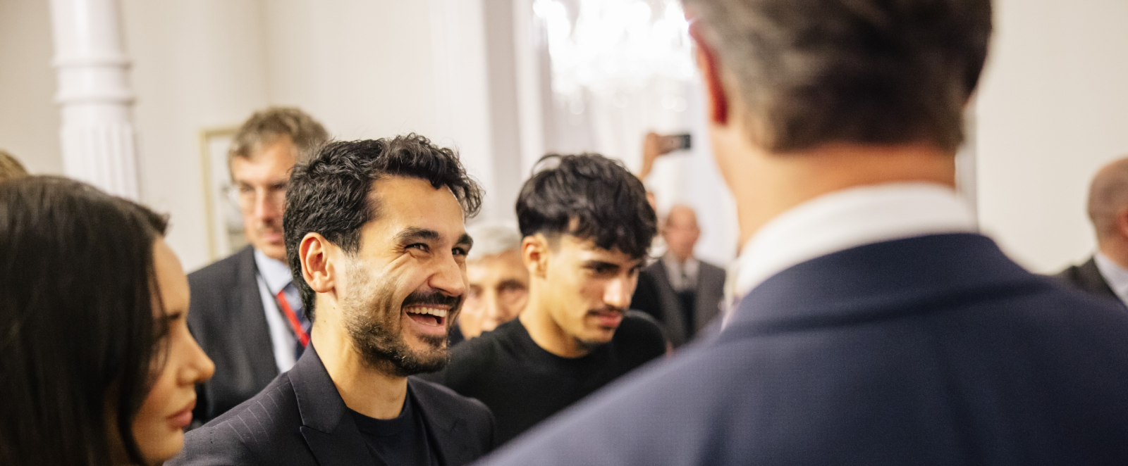 Ministerpräsident Wüst mit dem Rücken zum Betrachter neben lachendem Illkay Gündogan