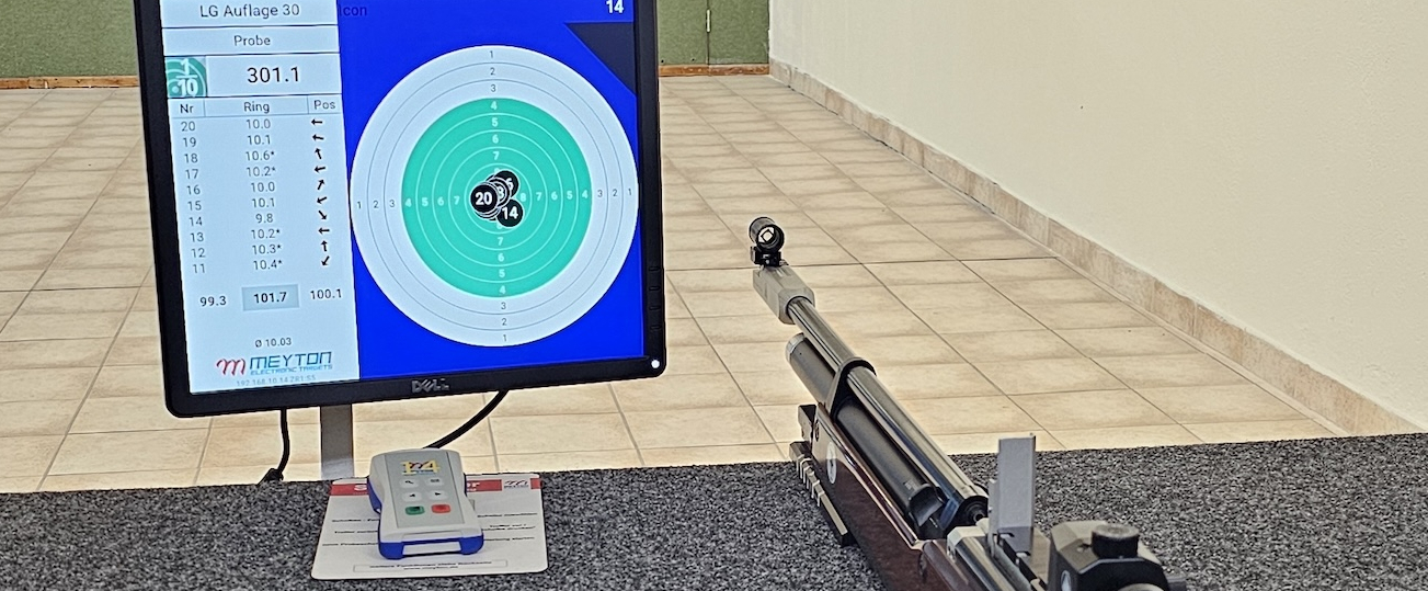 In einer Schießsportanlage liegt ein Sportgewehr neben einem Bildschirm mit der Anzeige des Ziels