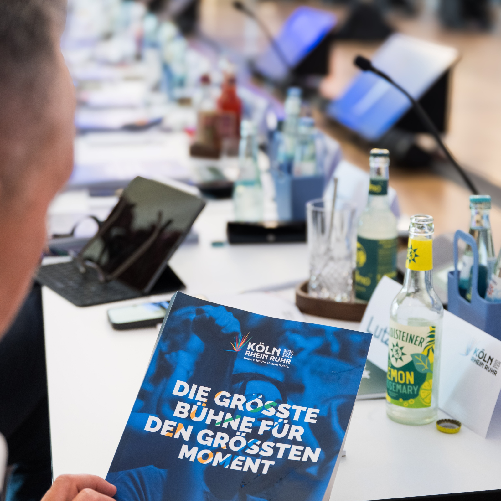 Ein Mann hält ein Booklet zu KölnRheinRuhr in der Hand, im Hintergrund ein langer Arbeitstisch