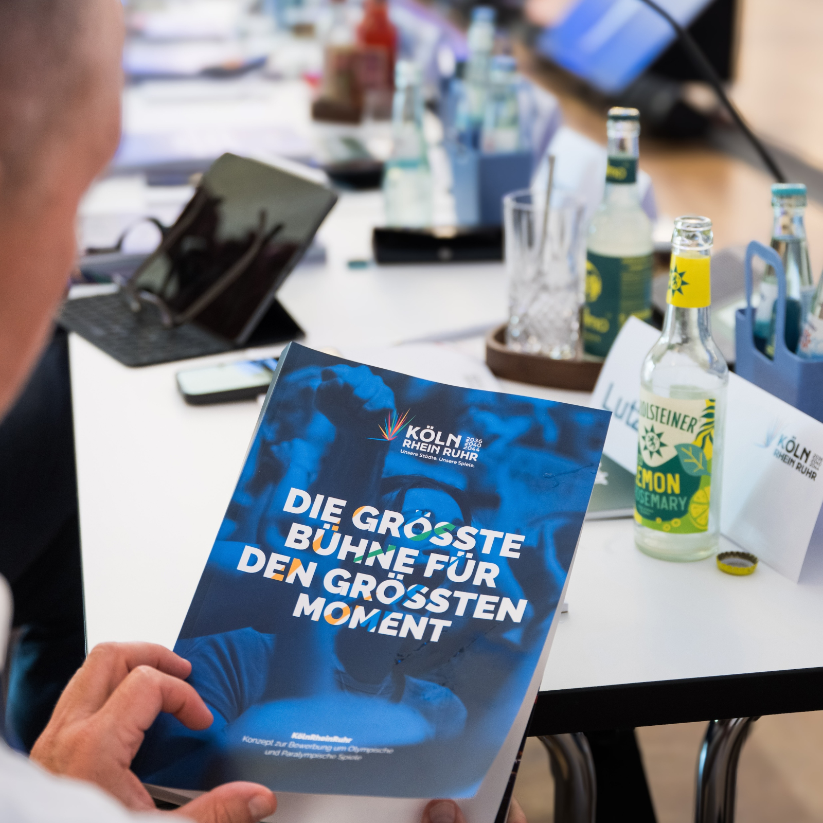 Profil eines Mannes, der das Booklet KölnRheinRuhr in den Händen hält, im Hintergrund ein langer Arbeitstisch