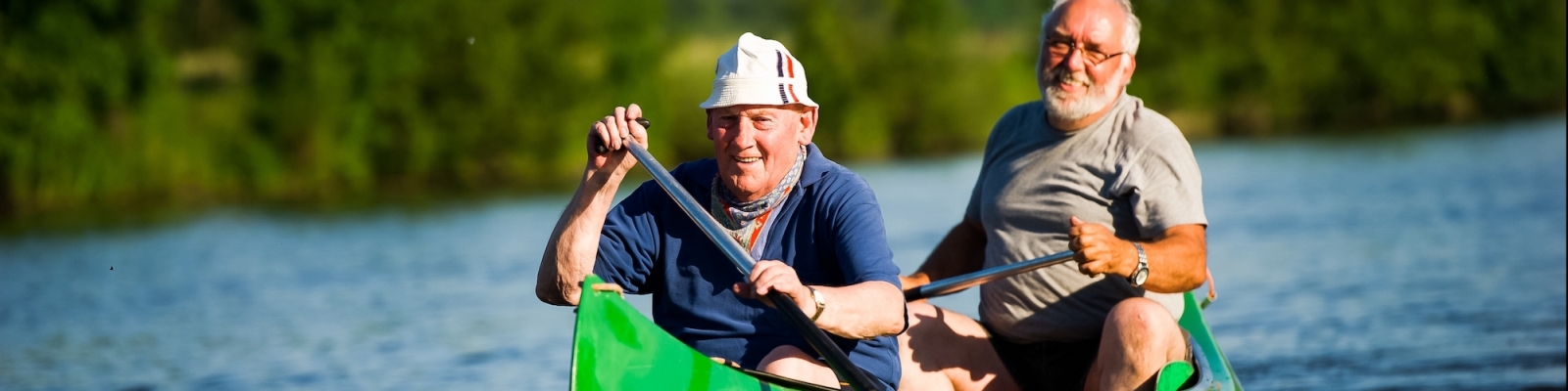 Zwei Senioren geimsam in einem grünen Kanu auf dem Wasser.